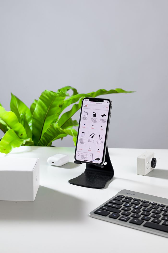 A smartphone on a stand with a keyboard and accessories on a white desk.