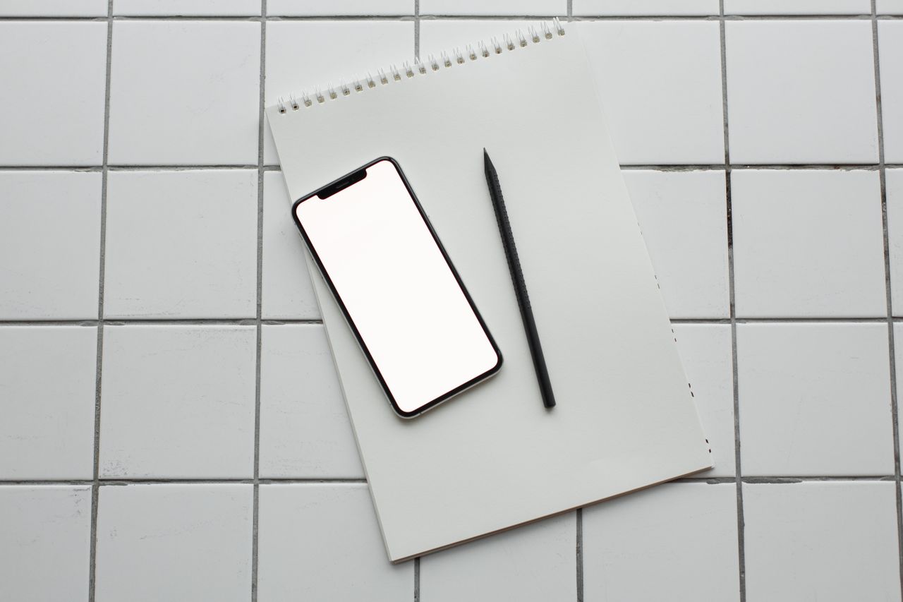Flatlay of a smartphone and notebook on a tiled surface, ideal for tech and productivity themes.