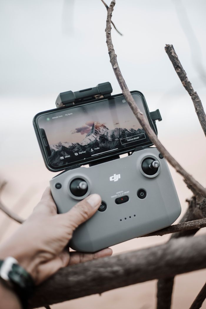 A person's hand holding a drone controller with a smartphone attached, showcasing an outdoor scene.